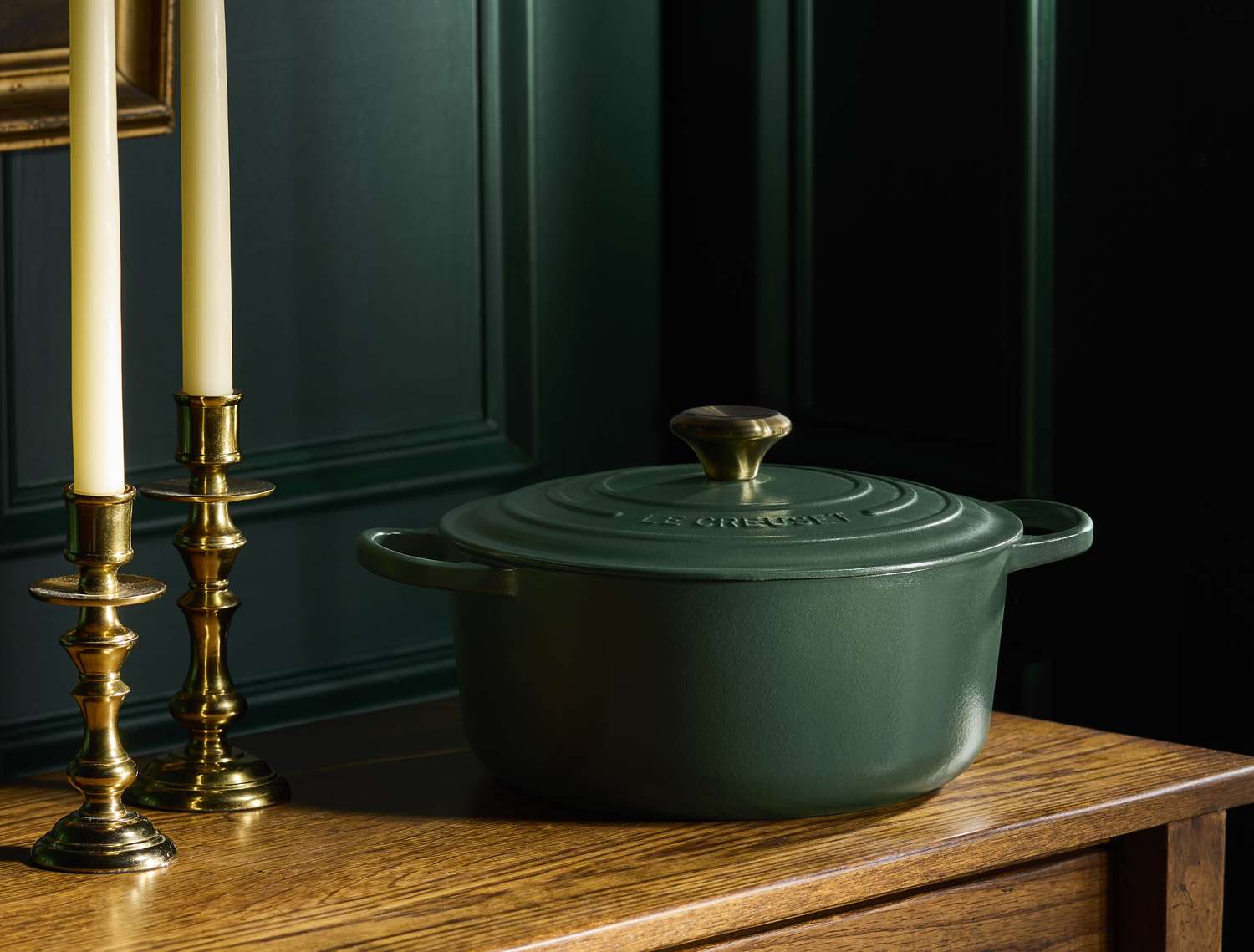 A green cast iron Dutch oven placed on a wooden surface near brass candlesticks
