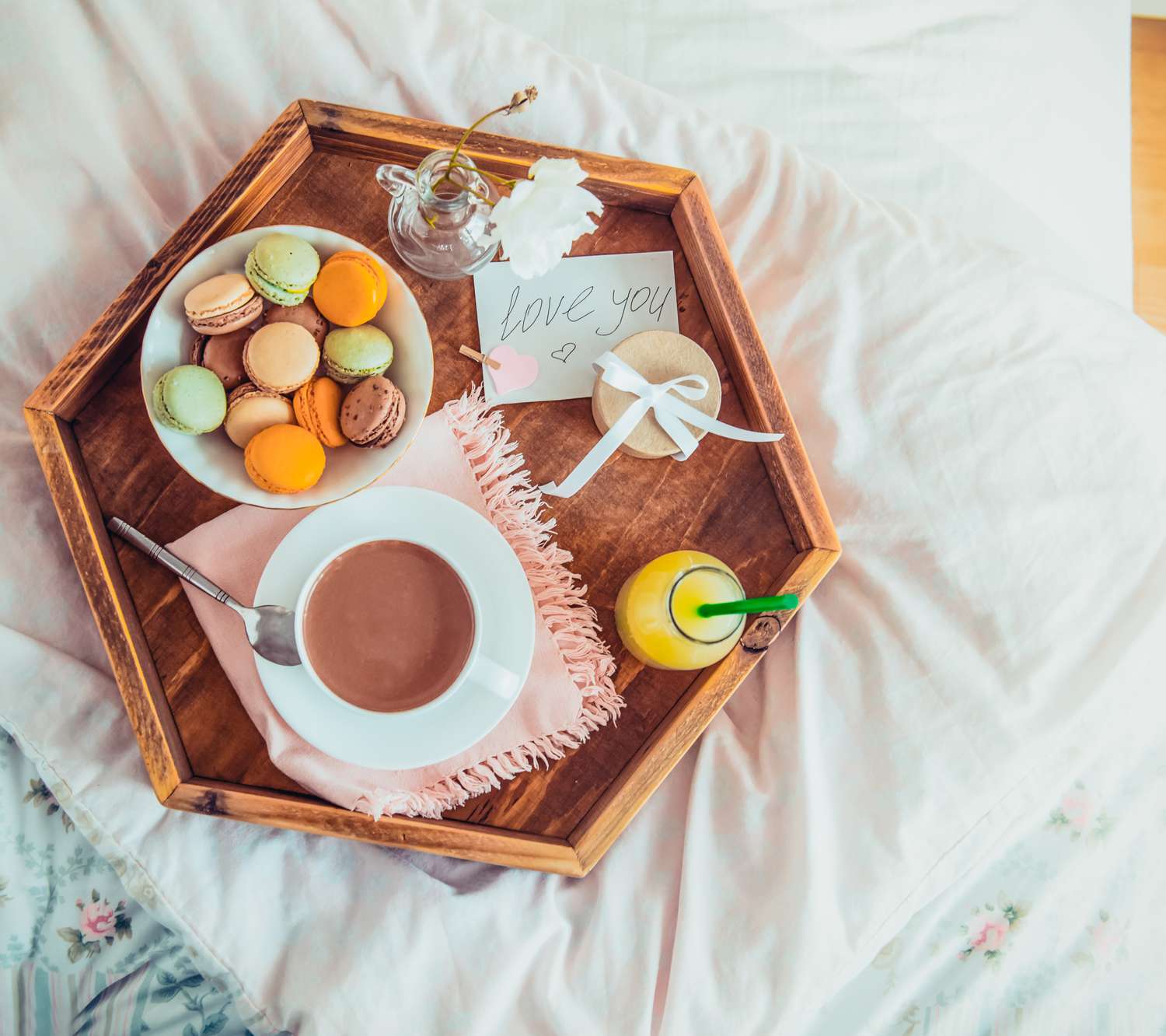 Tray with a mug macarons orange juice and a note resting on a bed