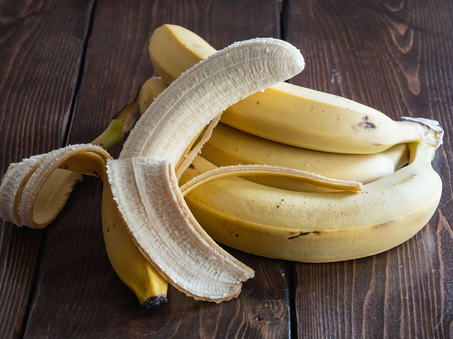 Several bananas, one partially peeled, on a wood surface