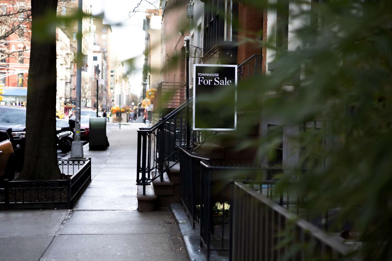 Residential street with a for sale sign visible near the entrance of a townhouse