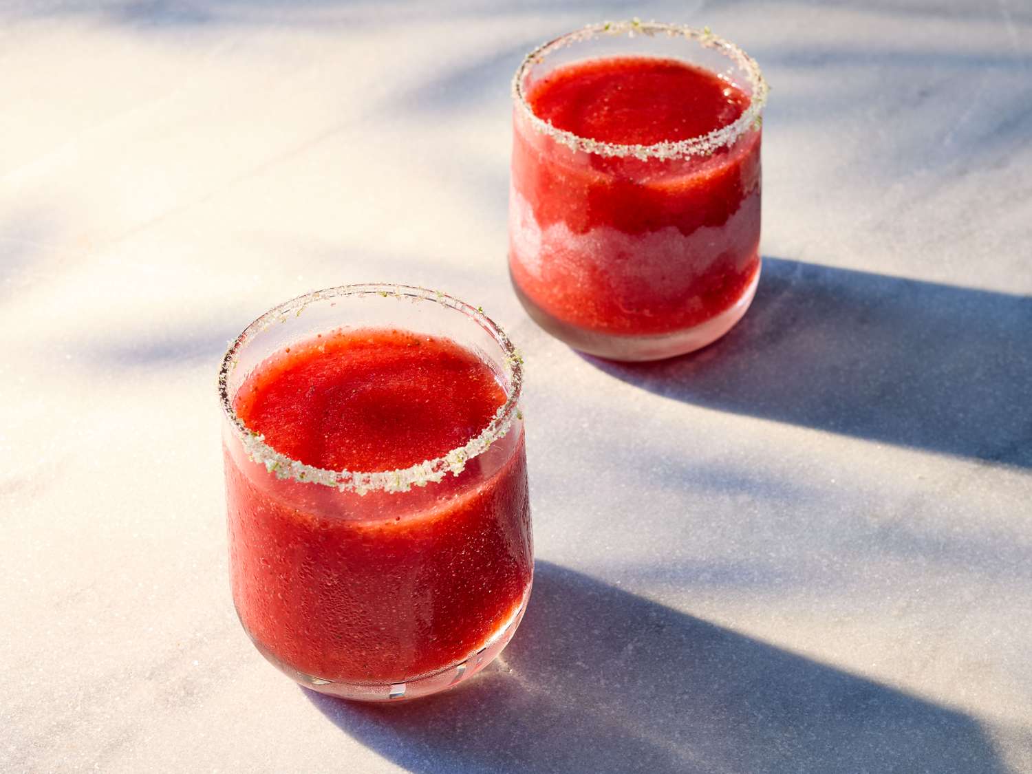 Two glasses of strawberry daiquiri on a light surface