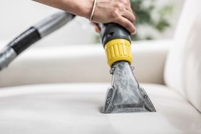 A hand operating a vacuum cleaning a piece of upholstered furniture