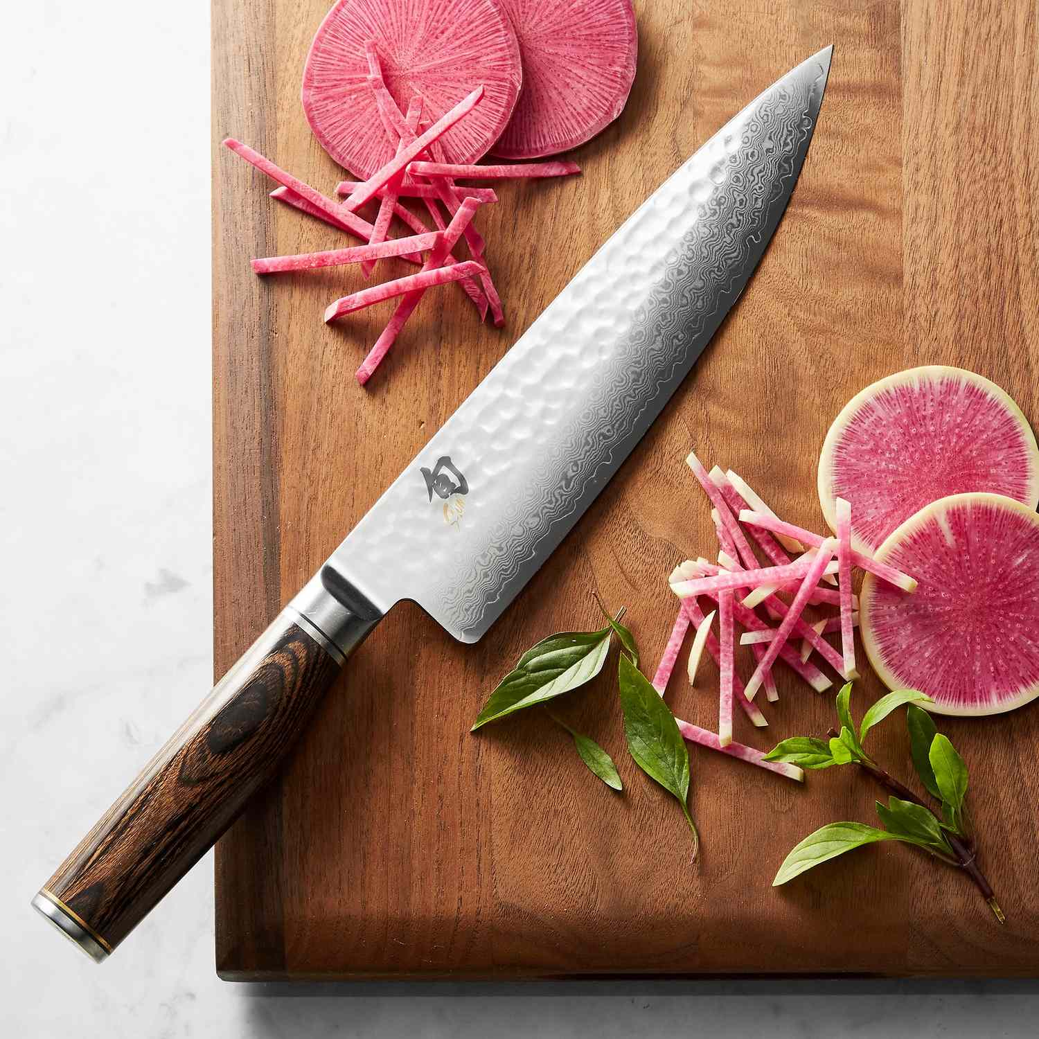 Chefs knife and sliced radishes on a wooden cutting board