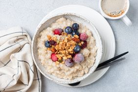 Breakfast bowl of porridge topped with berries and granola beside a cup of coffee and a napkin