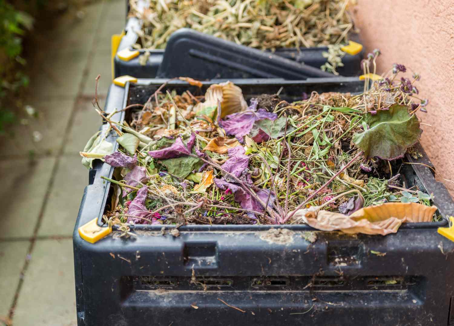 Compost bins filled with plant and organic waste set on a paved surface