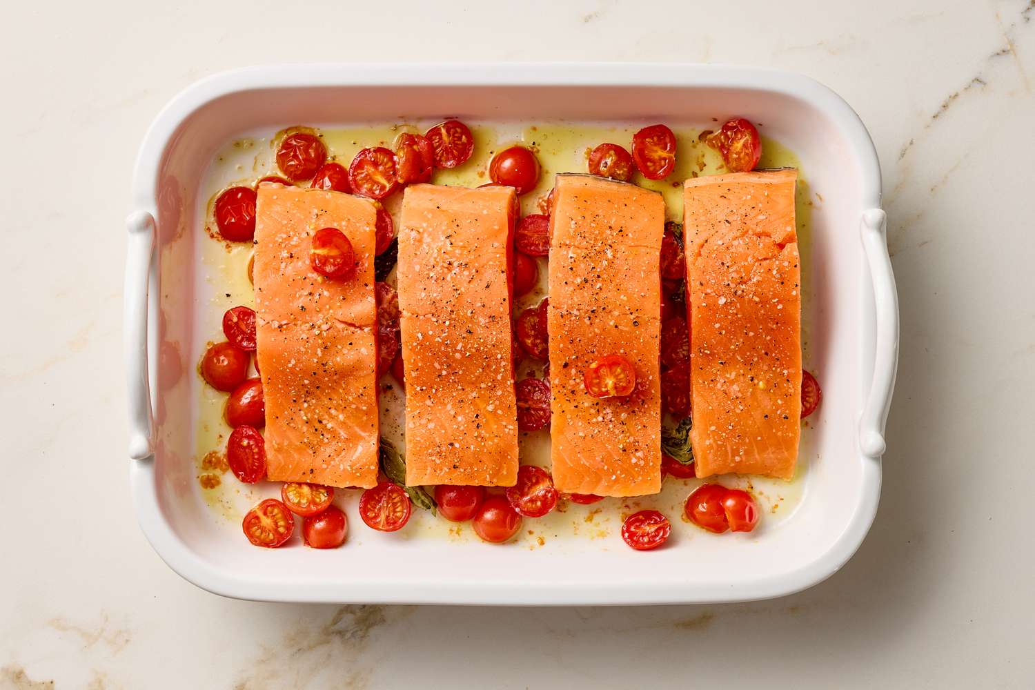 Four pieces of salmon placed in a baking dish with cherry tomatoes around them