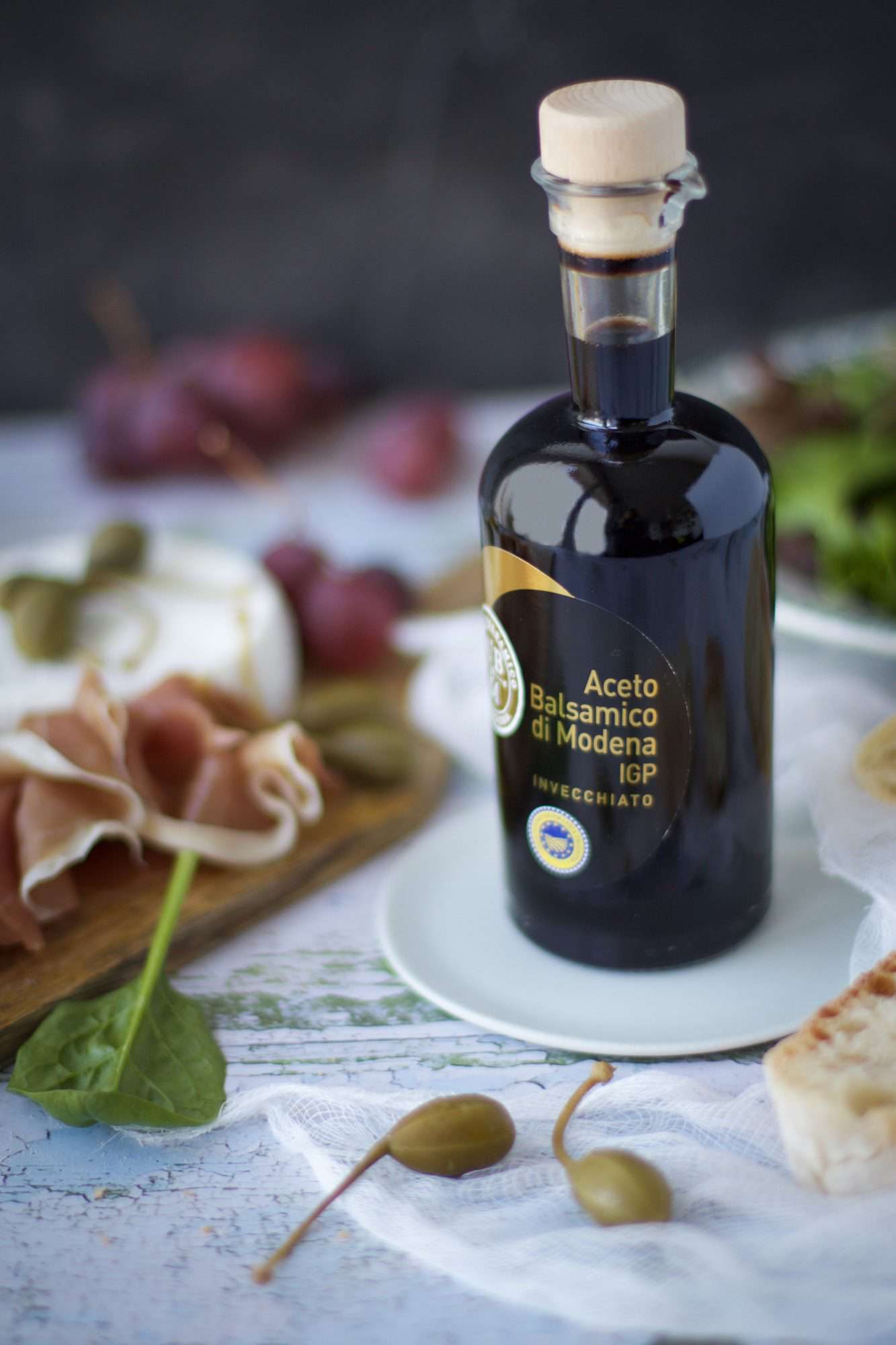 bottle of balsamic vinegar with proscuitto, caper berries, and bread