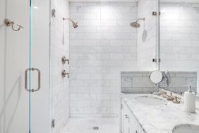 A modern bathroom with a marble countertop glass shower enclosures and tiled walls