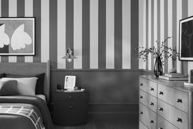 A bedroom with striped walls a bed a nightstand and a dresser with decor items