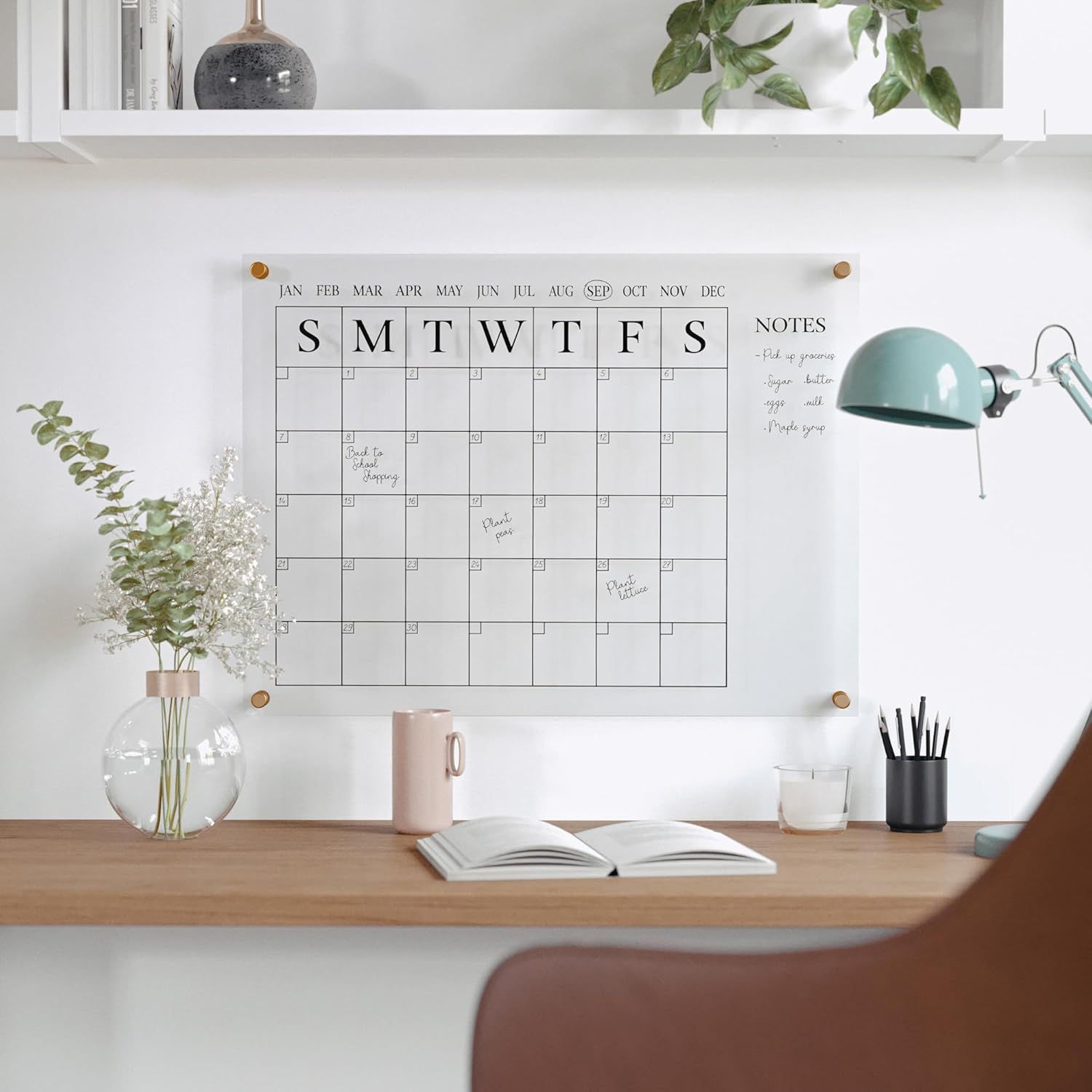 A home office desk setup with a wallmounted dryerase calendar and stationery items