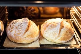 Two loaves of sourdough bread baking in an oven featuring decorative scoring on the surface