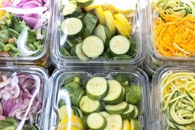Assorted plastic containers filled with precut vegetables including zucchini slices and spiralized vegetables