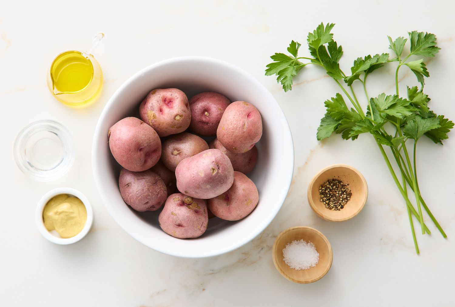 Ingredients for a Dijon potato salad including potatoes, mustard, vinegar, oil, salt, pepper, and fresh parsley