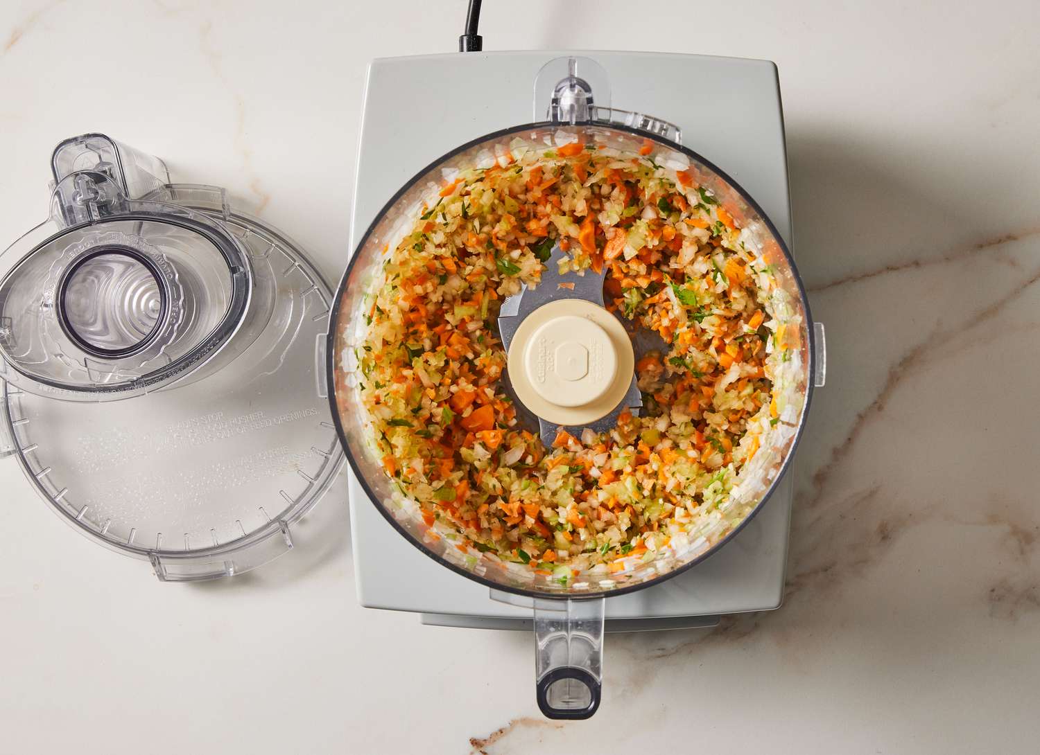 overhead view of a food processor with chopped carrots and herbs