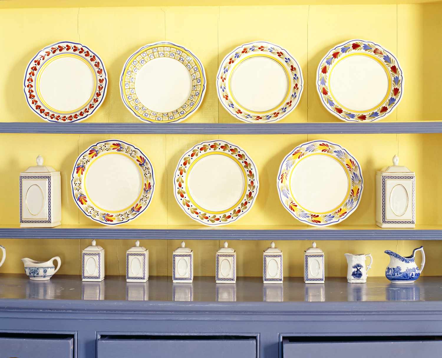 A set of colorful decorative plates displayed on shelves along with containers and pitchers