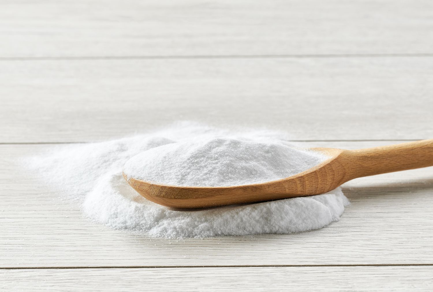 A wooden spoon resting on a pile of baking soda on a light wood surface