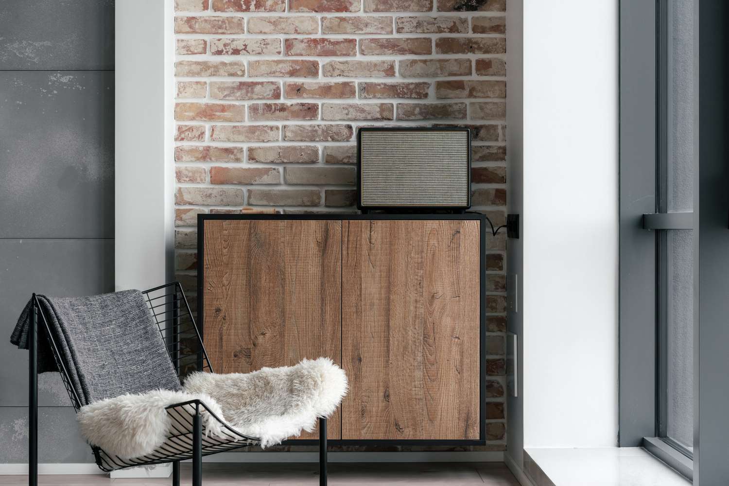 A chair with a blanket next to a wooden cabinet against a brick wall
