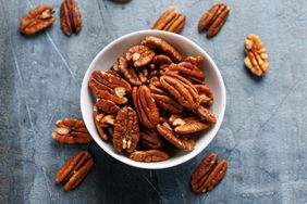 A bowl filled with pecan nuts on a textured surface