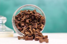 Dog treats in a glass container some spilling onto the surface