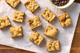 Chocolate chip cookie bars arranged on parchment paper next to a bowl of chocolate chips
