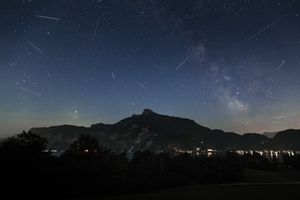 Night sky with a meteor shower silhouetted mountains with distant lights below