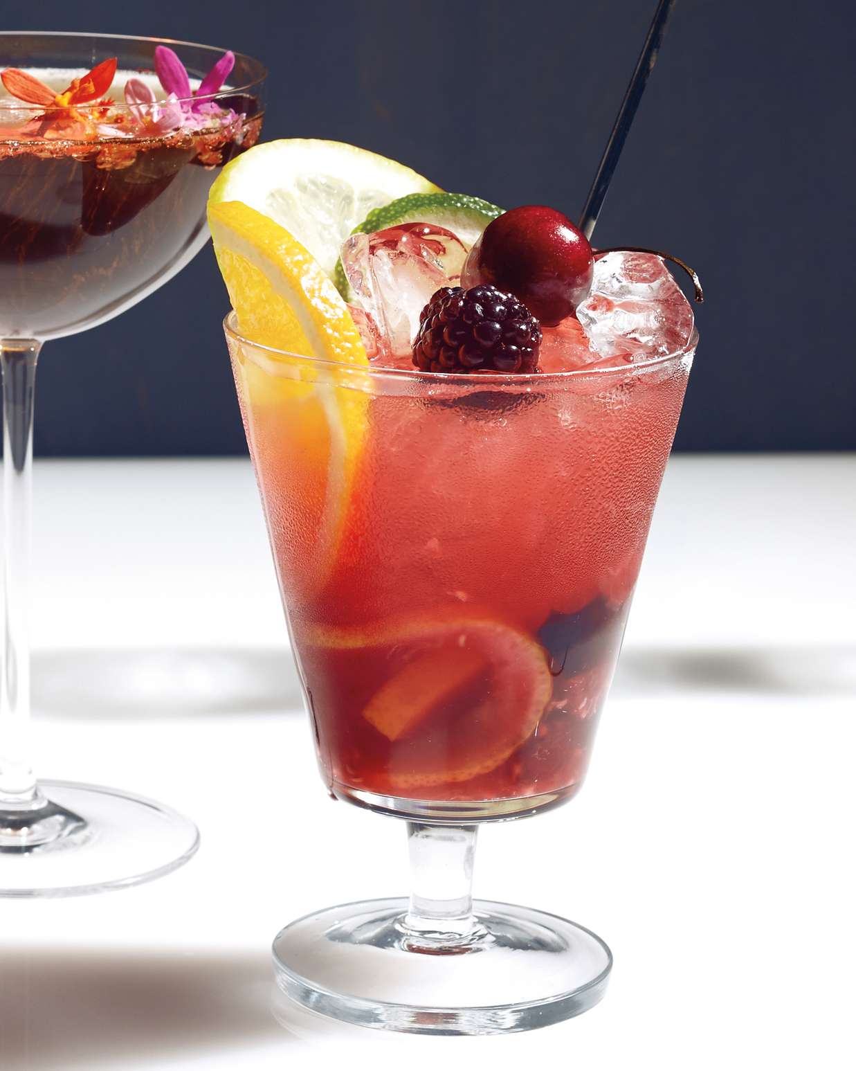 fruity pink cocktail with slices of lemon and lime and blackbery and cherry on top