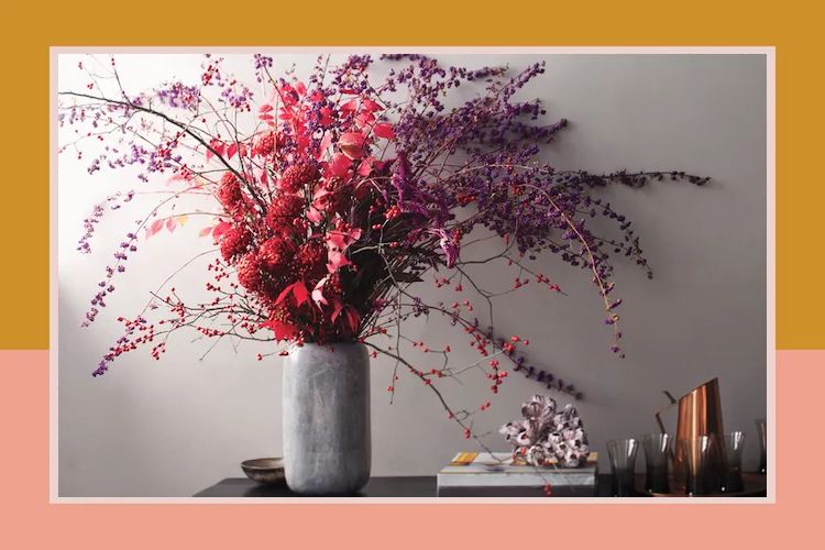 Vase with floral arrangement on a table accompanied by stacked books and decorative items