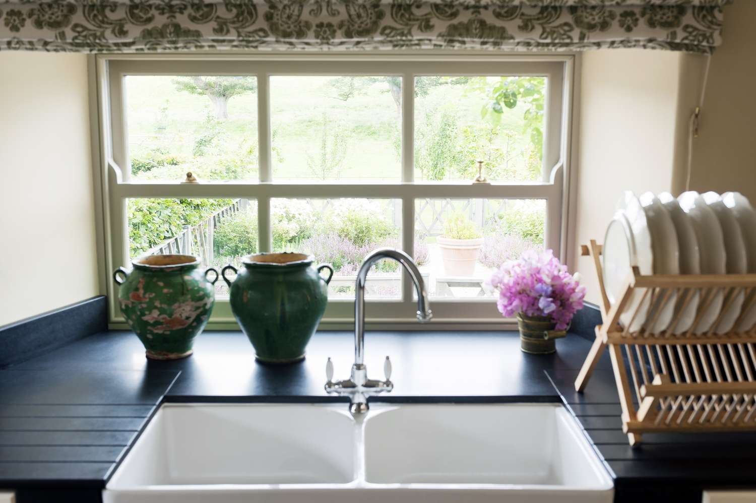 Kitchen sink with a window double sink with green decorative vases flowers and a dish rack on the counter