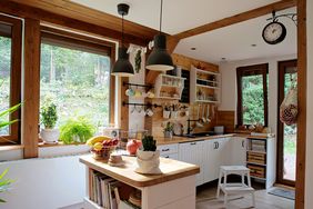 A cozy kitchen with wooden accents, a central island, and large windows overlooking greenery, shelves holding kitchen accessories