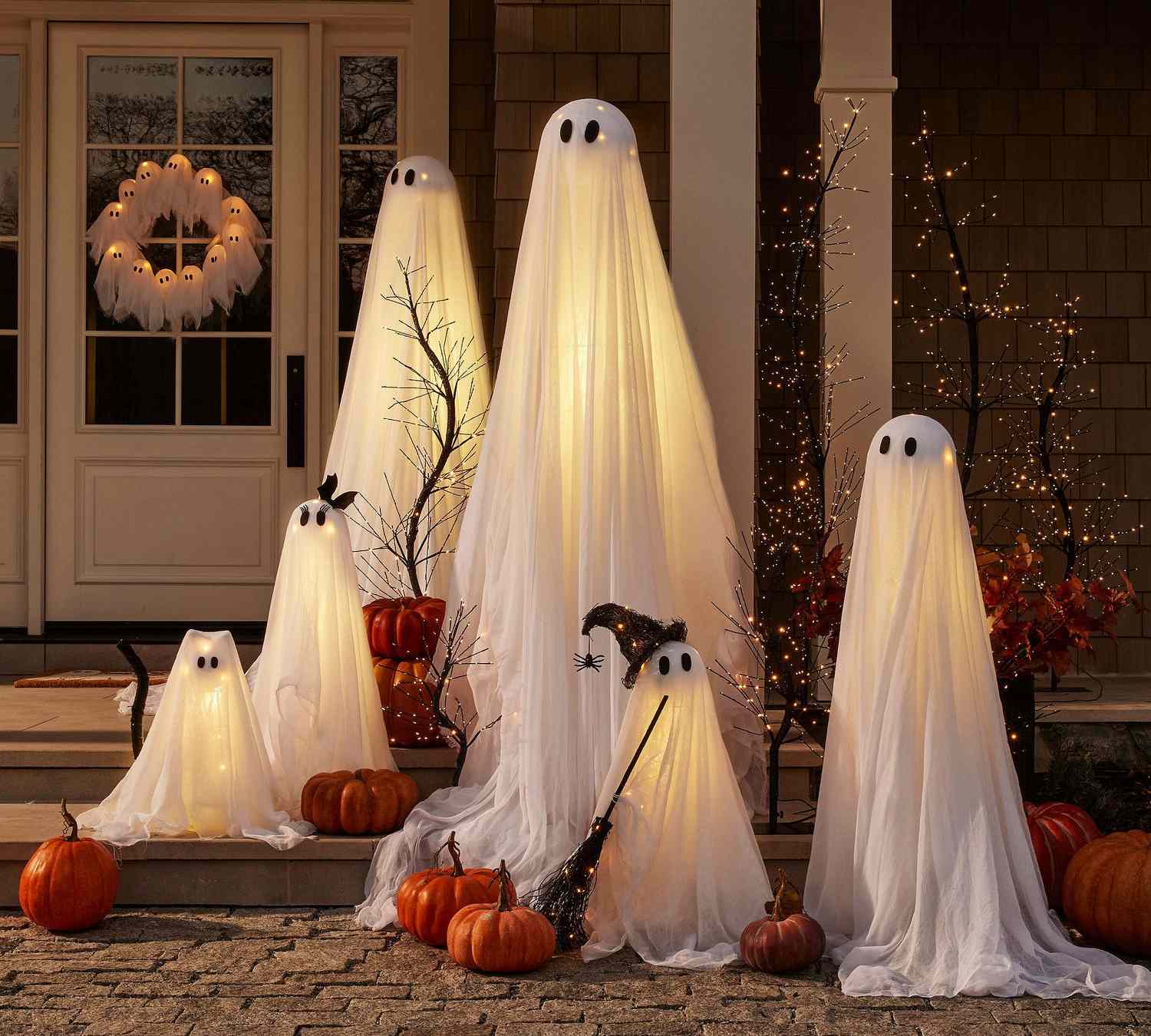 Halloween decorations featuring glowing ghost figures surrounded by pumpkins on a porch
