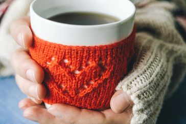 Red Knitted woolen cup with heart pattern in female hands