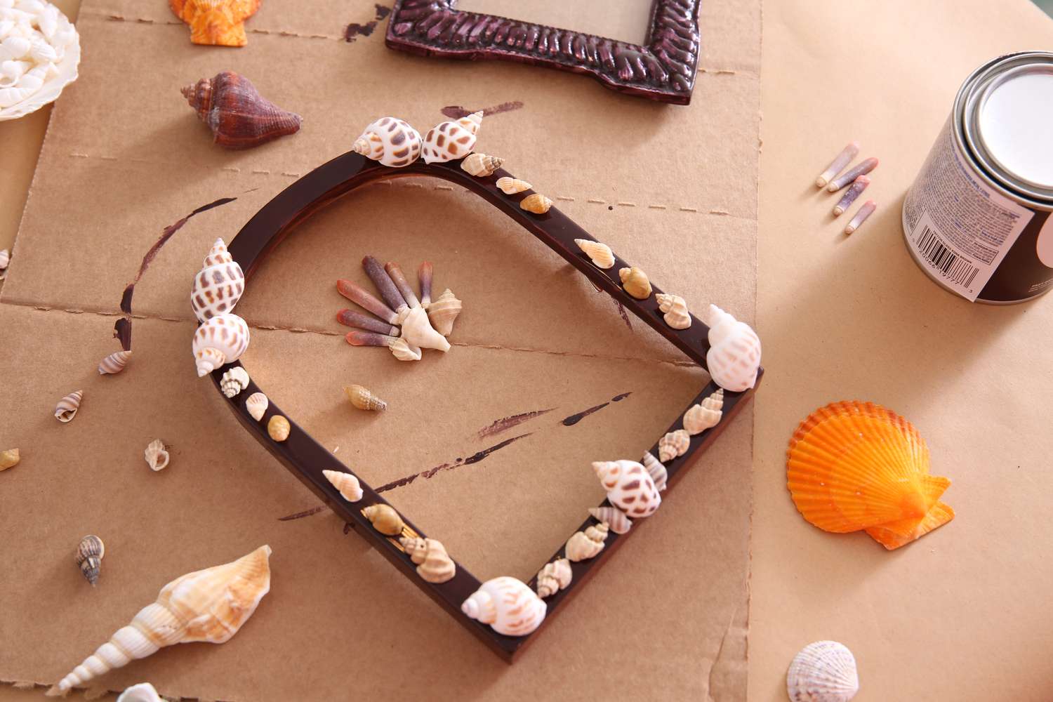 A photo frame being decorated with shells on a craft workspace