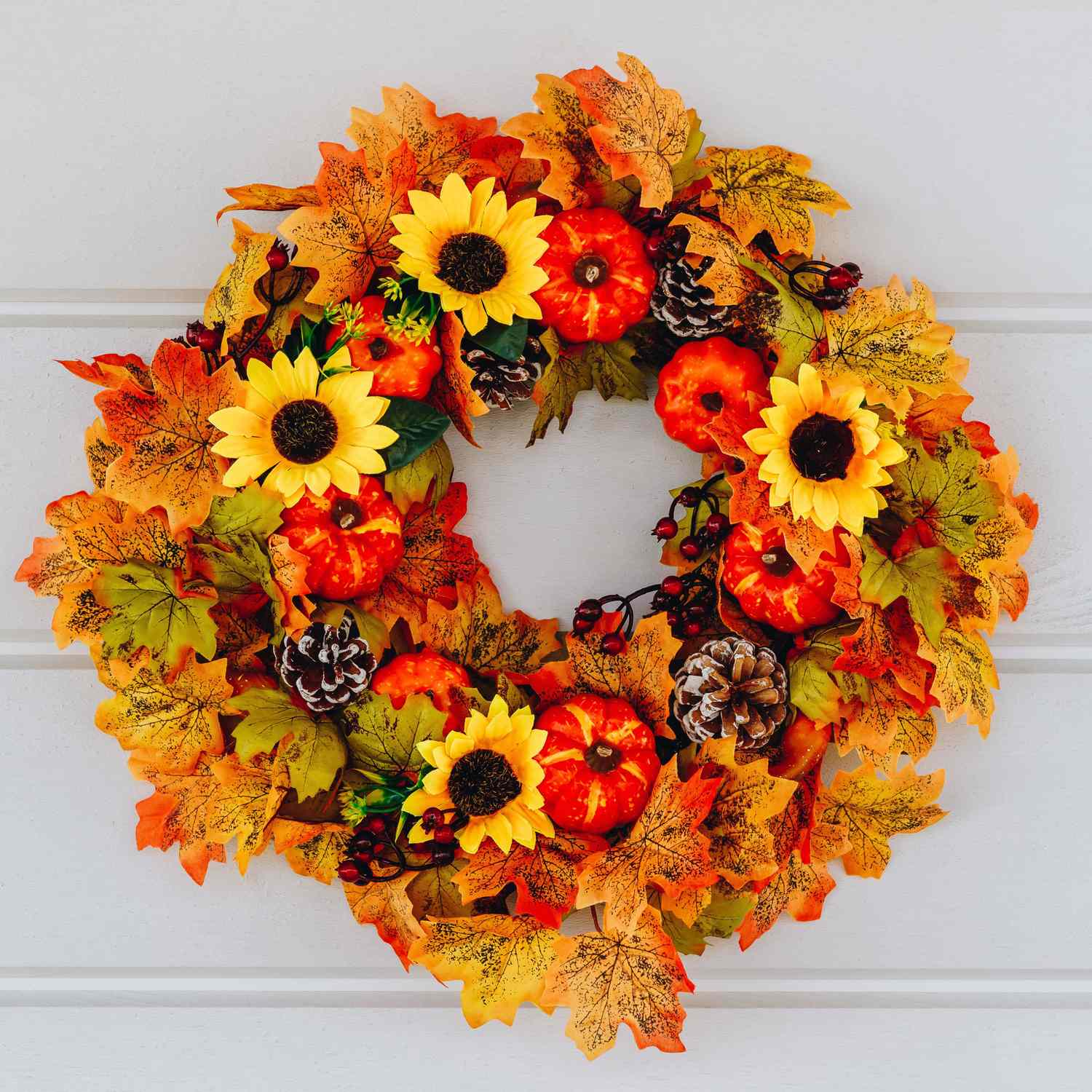 A fallthemed wreath with artificial flowers leaves pinecones and small pumpkins arranged in a circular pattern