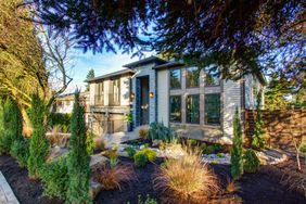 New construction home exterior with perfectly landscaped front yard boasts stone pathway, flower beds, decorative plants and trees.