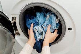 Person putting jeans into the drum of a washing machine, front view. Washing dirty jeans in the washer