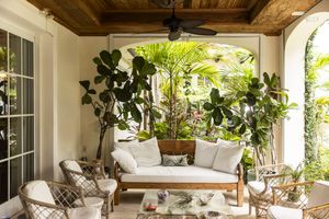 Cozy veranda seating area with a sofa chairs and a ceiling fan surrounded by lush tropical plants