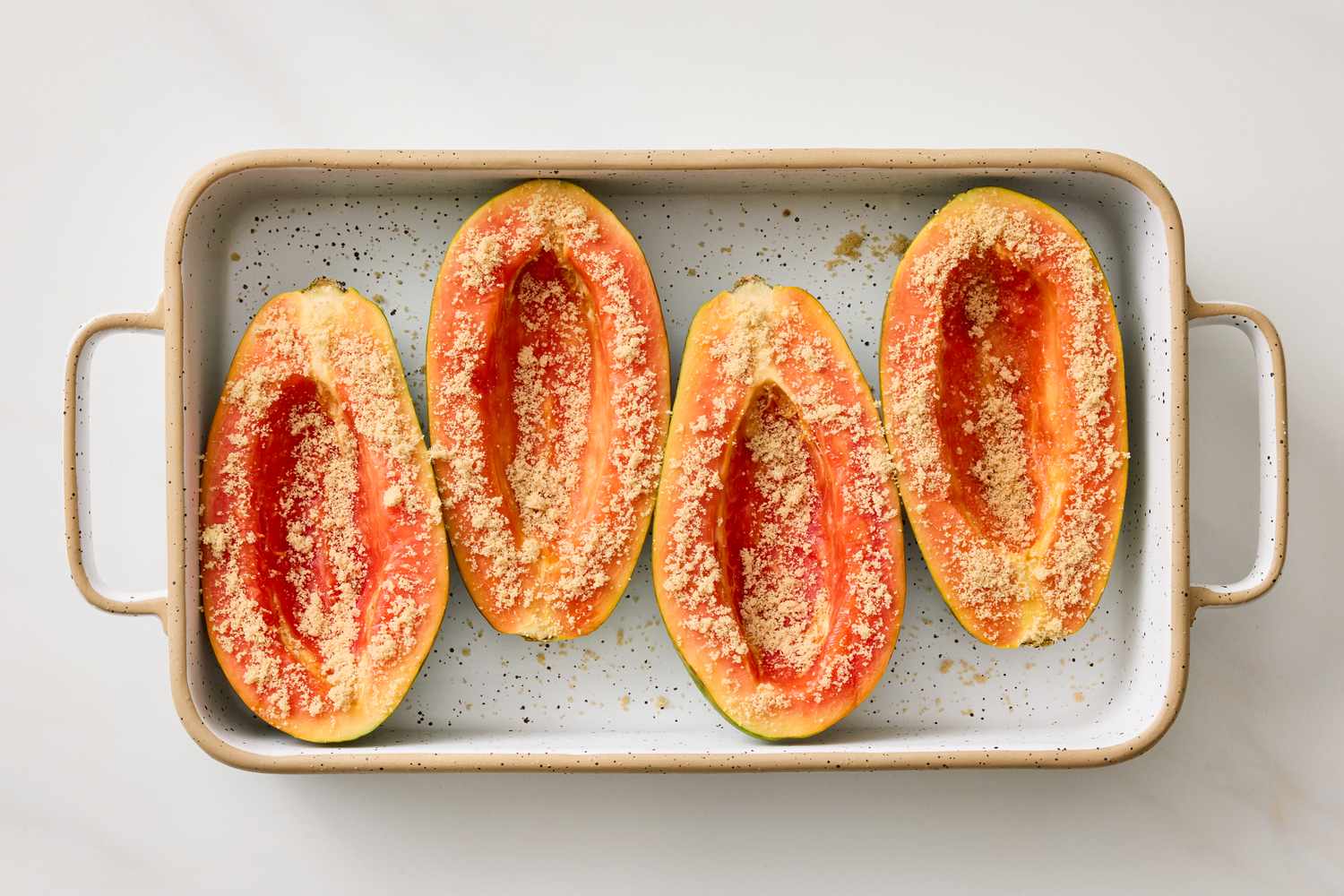 Halved papayas topped with brown sugar in a baking dish