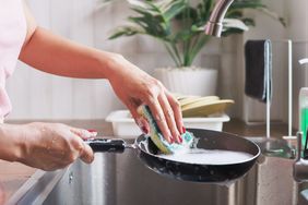 A person using a sponge to wash a frying pan in a kitchen sink