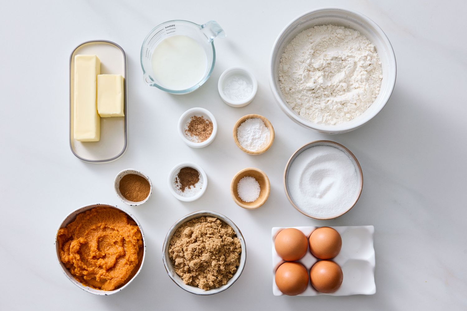 Ingredients for pumpkin bread arranged on a table including flour eggs pumpkin pure brown sugar and butter
