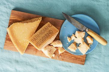 Pieces of Parmigiano Reggiano cheese on a wooden board with a knife on a blue plate