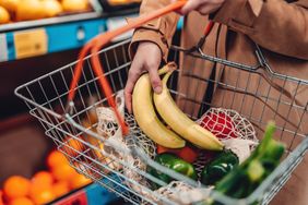 Person carrying a shopping basket containing bananas and other fruits and vegetables