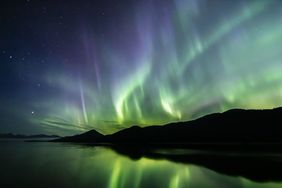 Aurora borealis over a silhouetted landscape with a water reflection depicting a natural phenomenon in the night sky