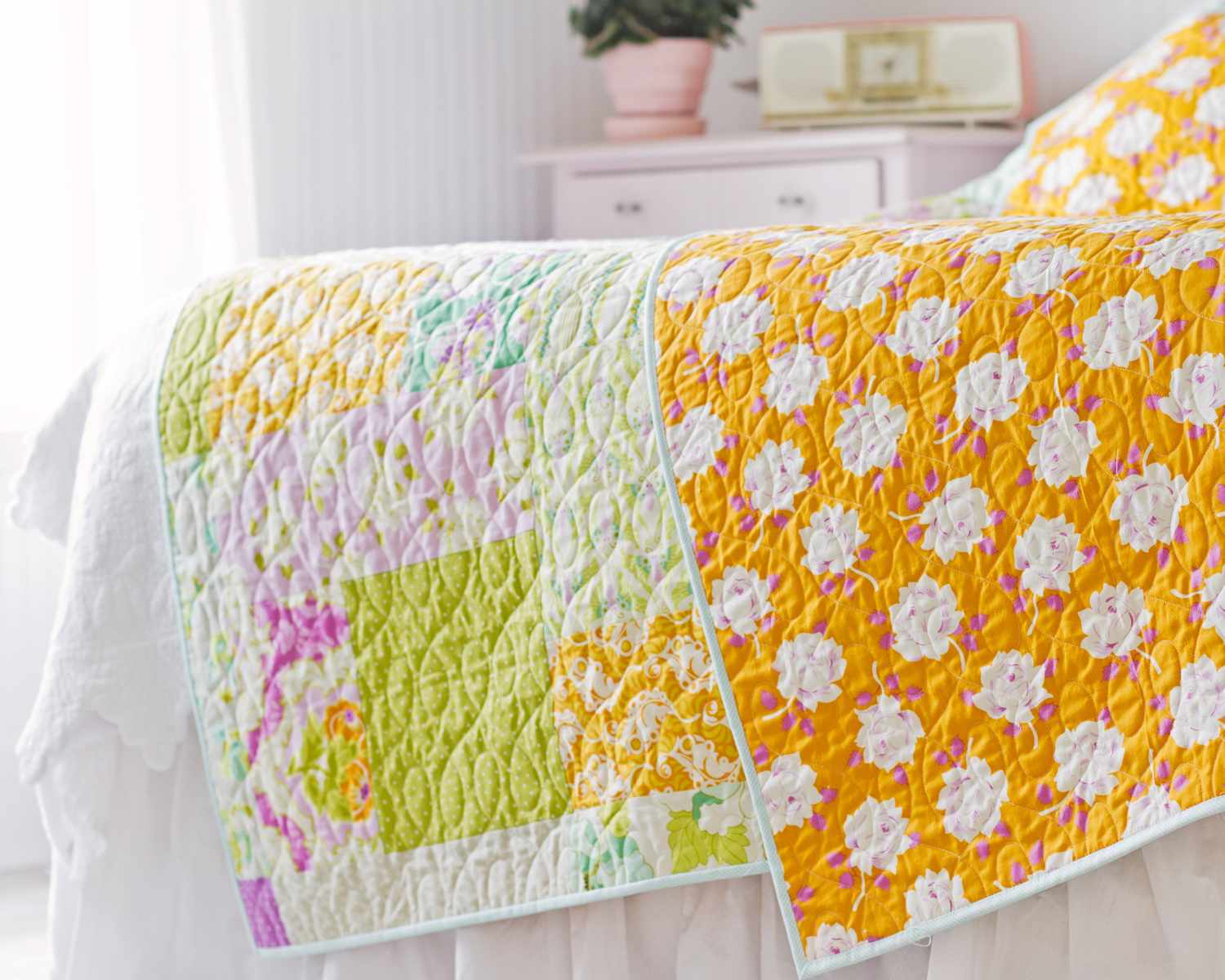 Quilt spread on a bed in a brightly lit room featuring a patchwork design with geometric patterns
