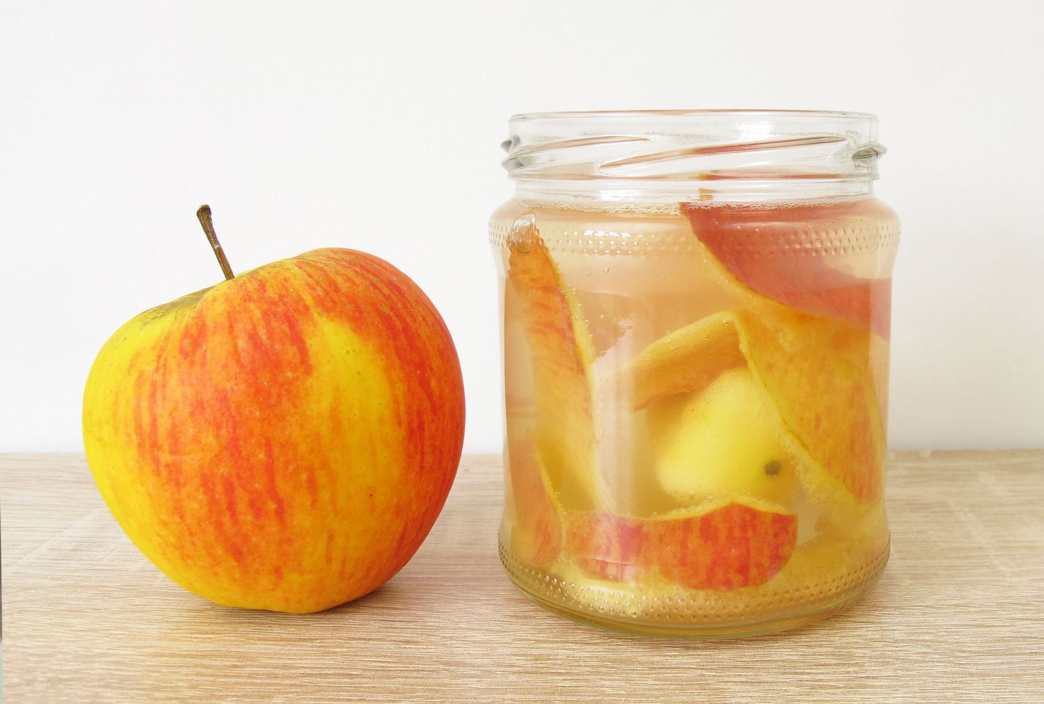 An apple and a jar containing apple cider vinegar with apple pieces