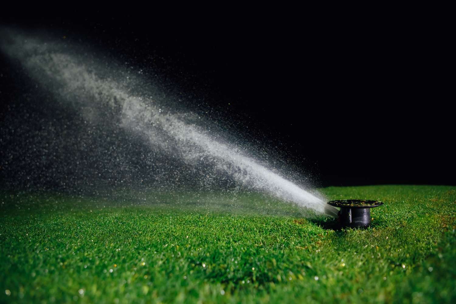 A lawn sprinkler spraying water over a grassy area at night