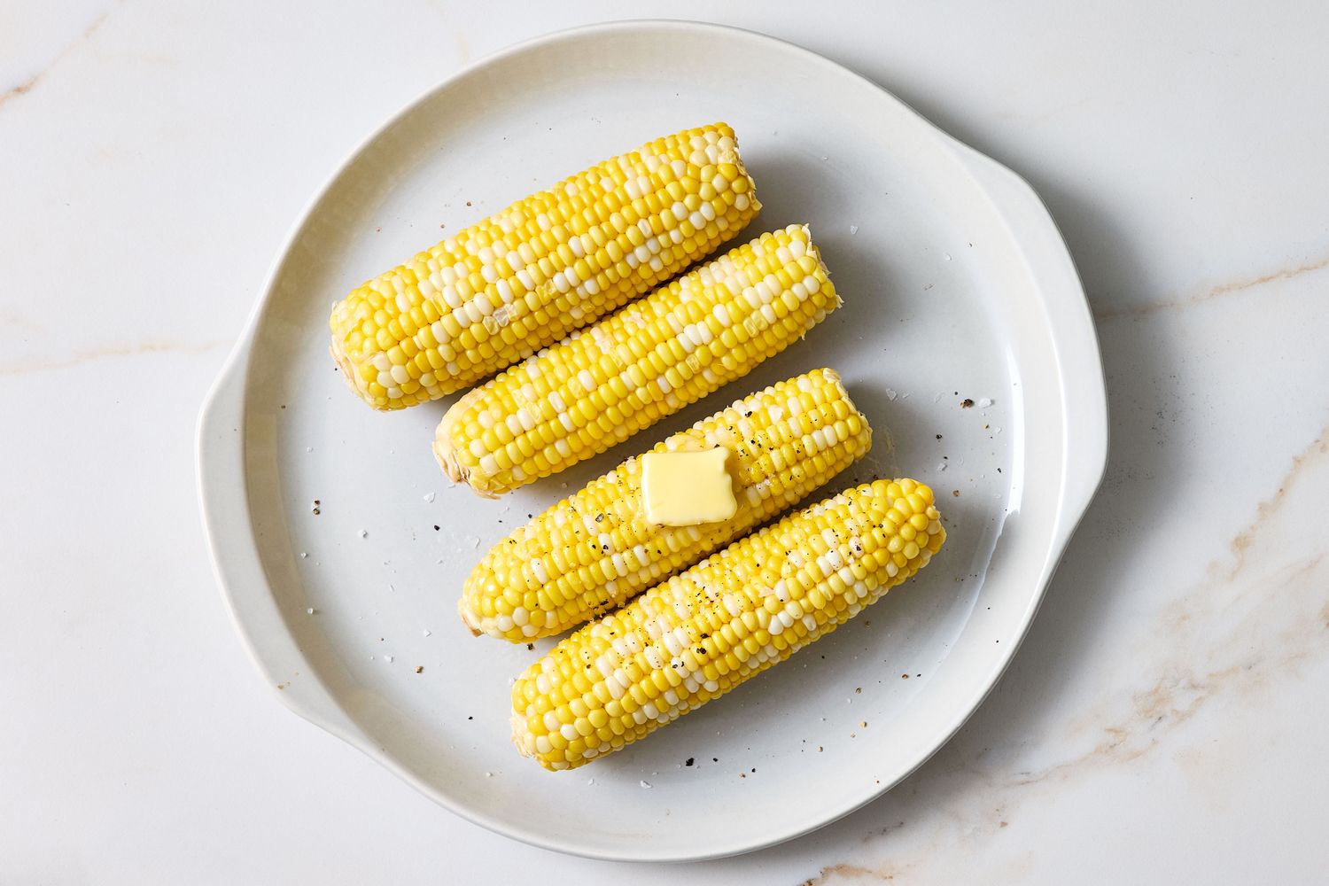 Cooked corn on the cob with a piece of butter on a plate