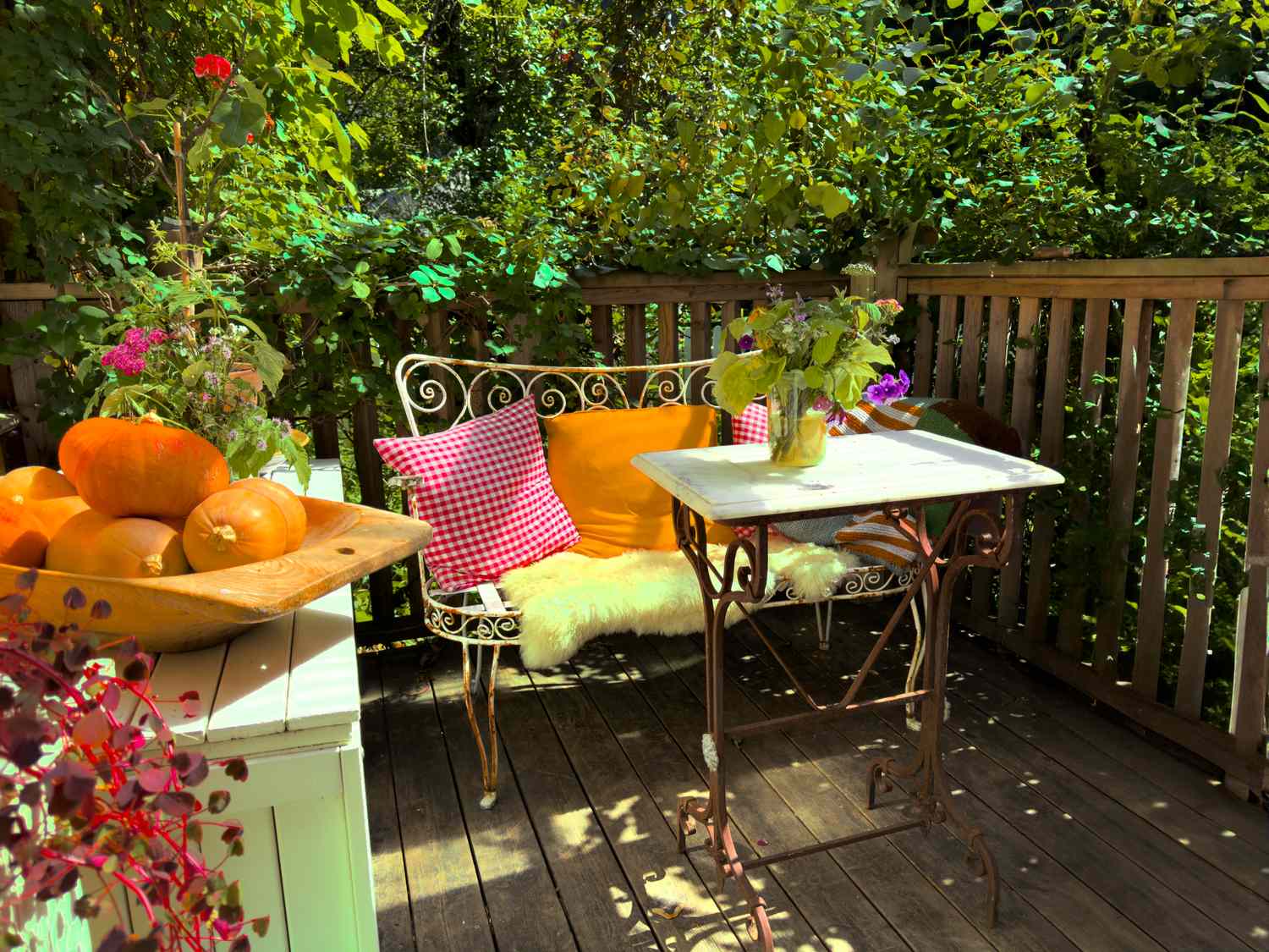 An outdoor seating area with a decorative bench table pumpkins and plants