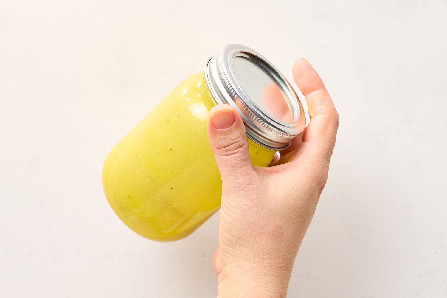A hand holding a jar of vinaigrette with a metal lid