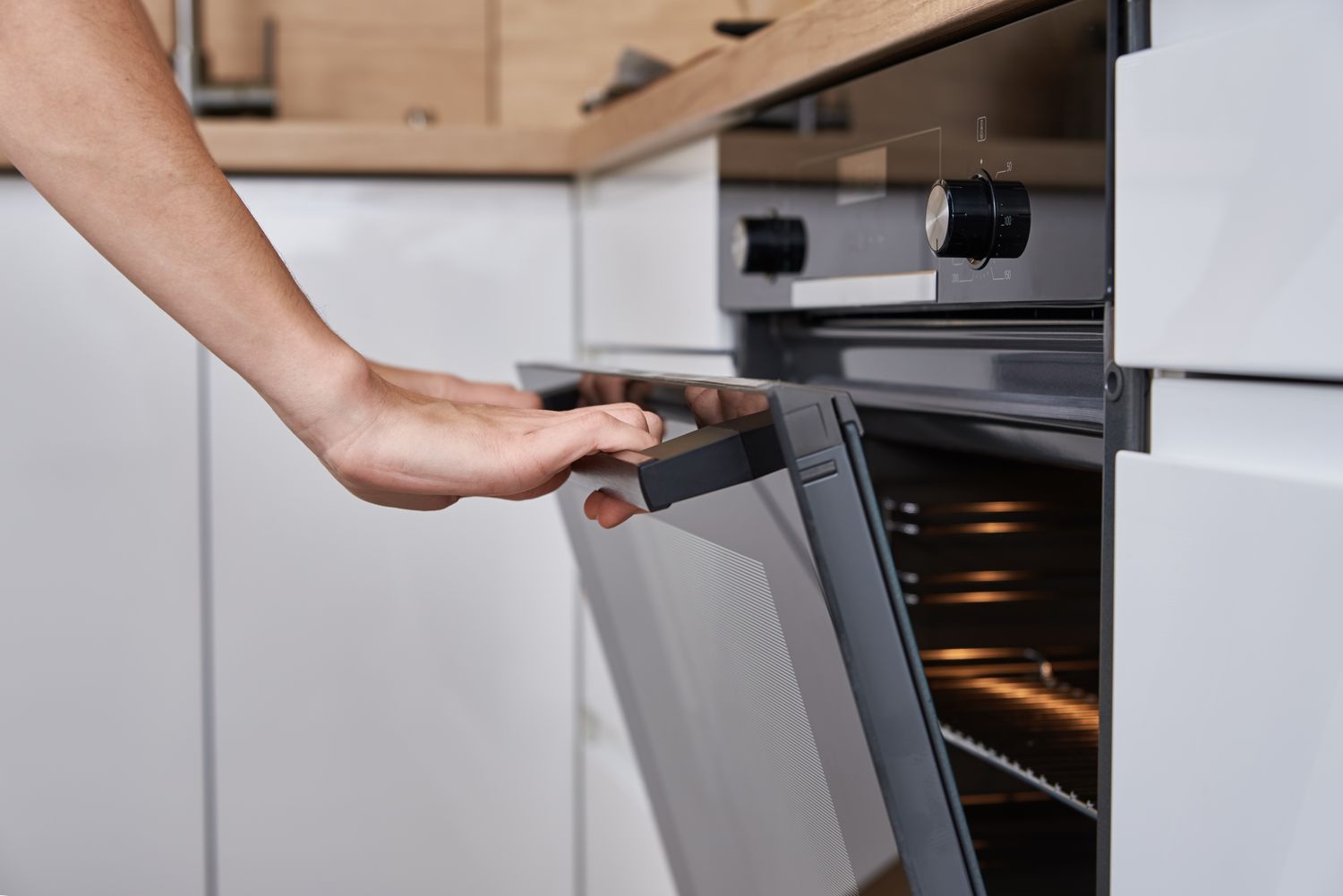 A person opening a modern oven in a kitchen environment
