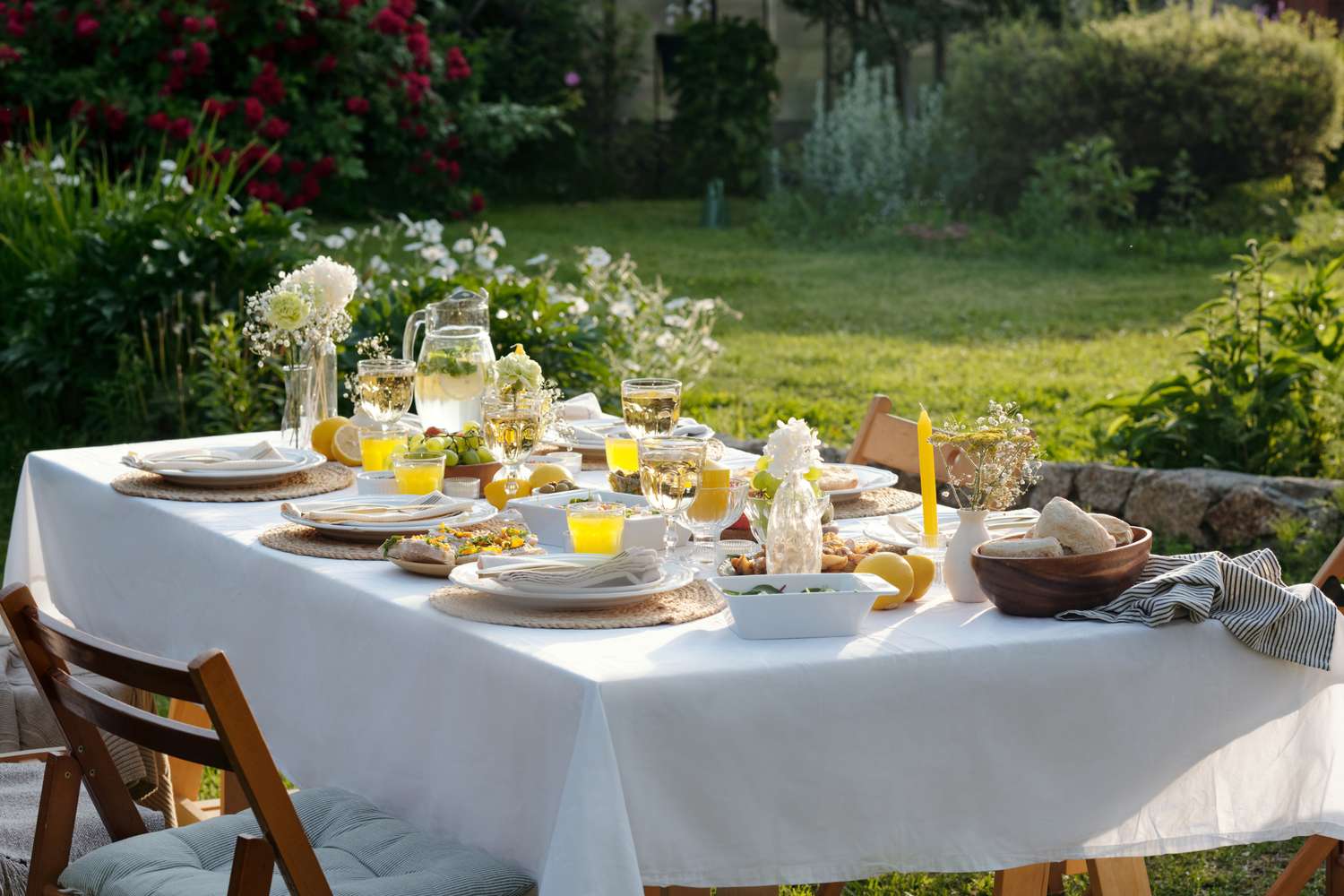 Outdoor dining table set with dishes glassware and floral decorations in a garden setting